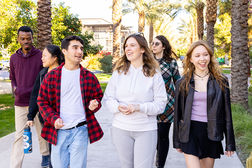 Six ASU students talk and laugh while walking down Palm Walk on the Tempe campus.